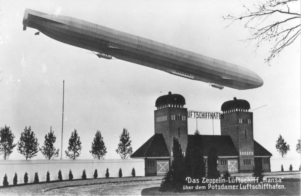 Schwarz-weiß Bild eines Gebäudes über dem ein Zeppelin schwebt.