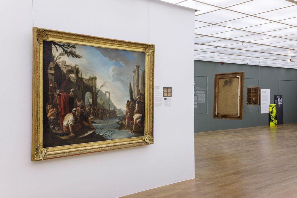 Ausstellungsansicht der Kunstausstellung im Zeppelin Museum, links ein großes Gemälde, rechts im Hintergrund die Rückseite von Bildern die von der Decke hängen.