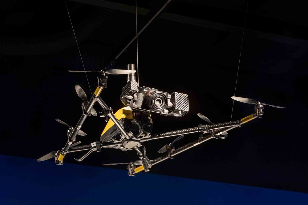Das Bild zeigt die Nahaufnahme einer Drohne, die von der Decke hängt. Vorne an der Drohne ist eine Kamera befestigt.