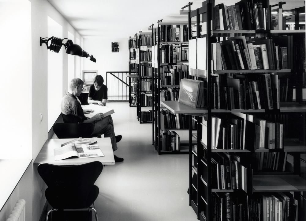 Der Blick in die Bibliothek zeigt zwei lesende Personen und gefüllte Bücherregale.