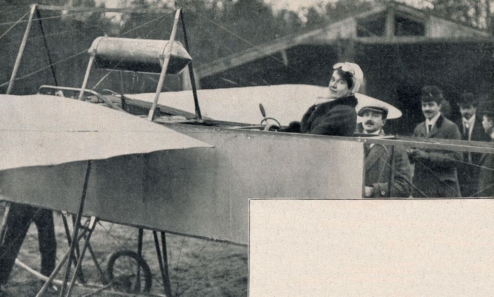 Die historische Aufnahme zeigt eine Frau, die in einem Flugzeug sitzt und in die Kamera schaut. Hinter ihr stehen vier Männer. 