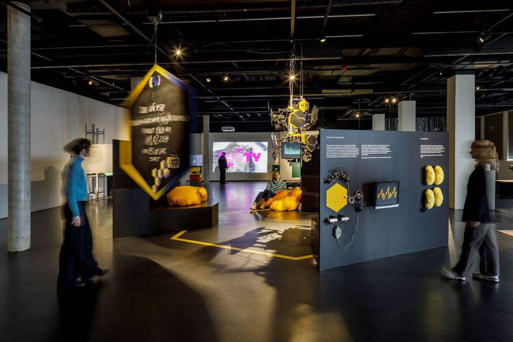 Menschen sitzen und laufen in der Ausstellung "Kryptomania. Die Verheißungen der Blockchain".