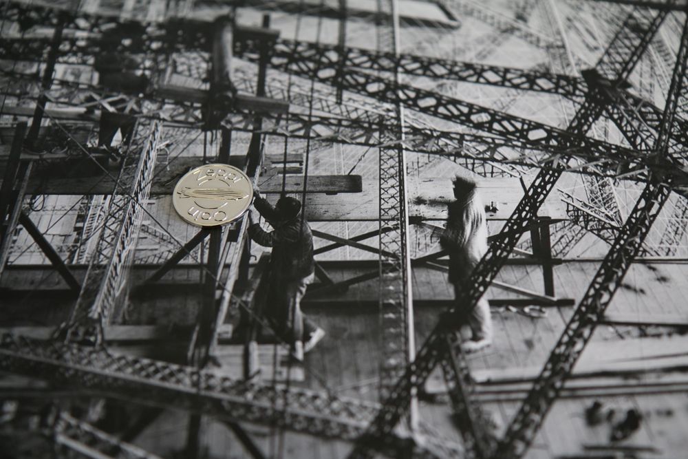 Historische Fotografie von arbeitenden Zeppelinern inmitten eines Luftschiffgerippes und ein daraufliegender Zeppi Coin.