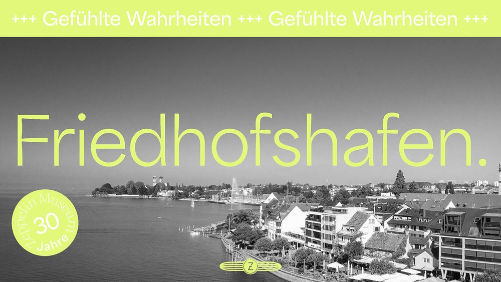 Schwarz-weiße Stadtansicht von Friedrichshafen, das Ufer vom Bodensee link im Bild. In grüner Schrift steht in der Bildmitte "Friedhofshafen".