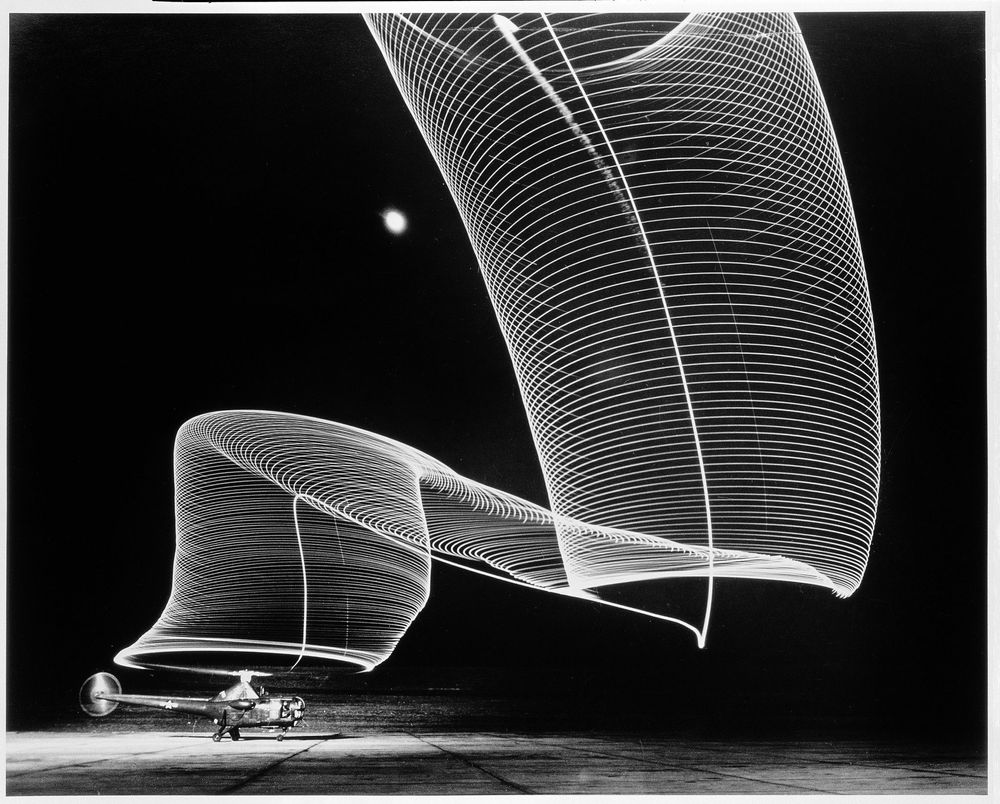 Die schwarz-weiß Fotografie zeigt eine Lichtspirale, die durch eine Langzeitbelichtung entstand. Unter der Spirale steht ein ein Flugzeug, von dem die Spirale auszugehen scheint. 