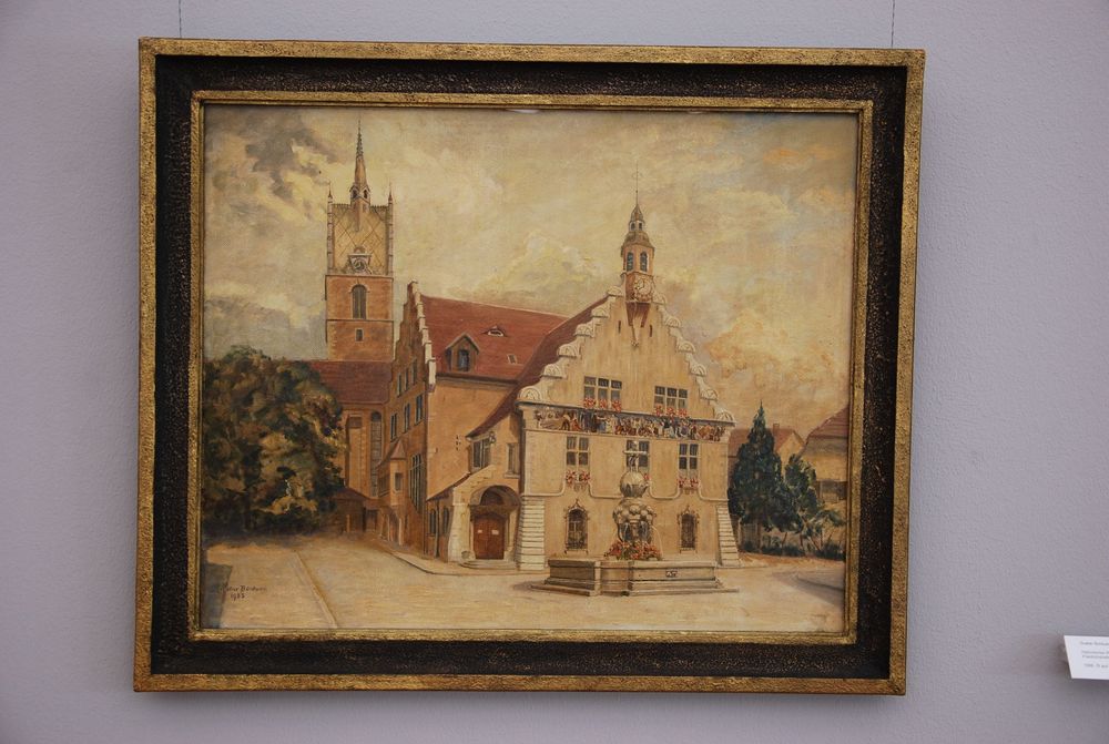 Ein Gemälde, das ein Haus zeigt, hängt an einer grauen wand.