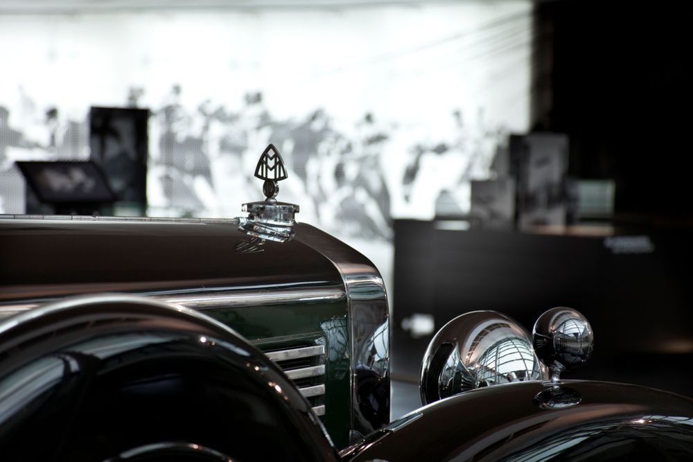 Nahaufnahme eines klassischen Maybach-Zeppelin-Automobils mit glänzendem Kühlergrill und verziertem Kühleremblem. Im Hintergrund ein unscharfes Wandbild und Vitrinen, sowie Monitore.