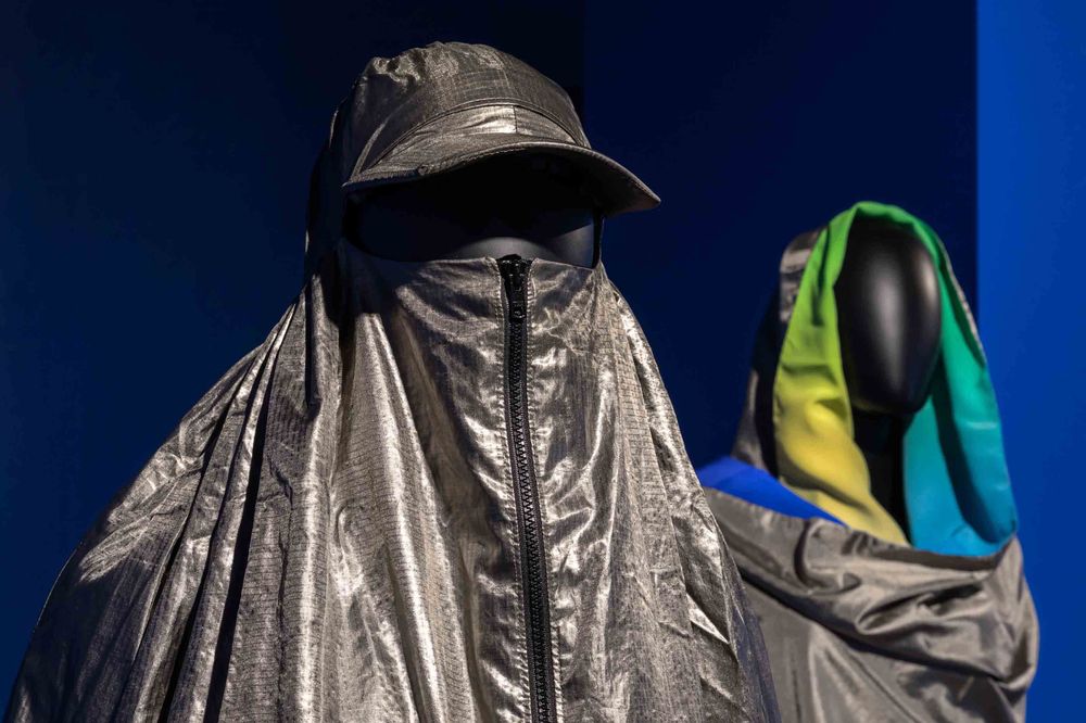 Zwei Schaufensterpuppen tragen graue Kleidung, an der sich Mützen und Kapuzen befinden.