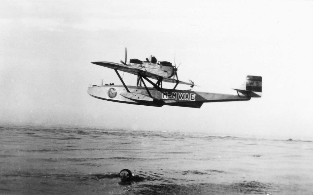 Die historische Aufnahme zeigt ein Flugzeug beim Start, im Flug über Wasser.