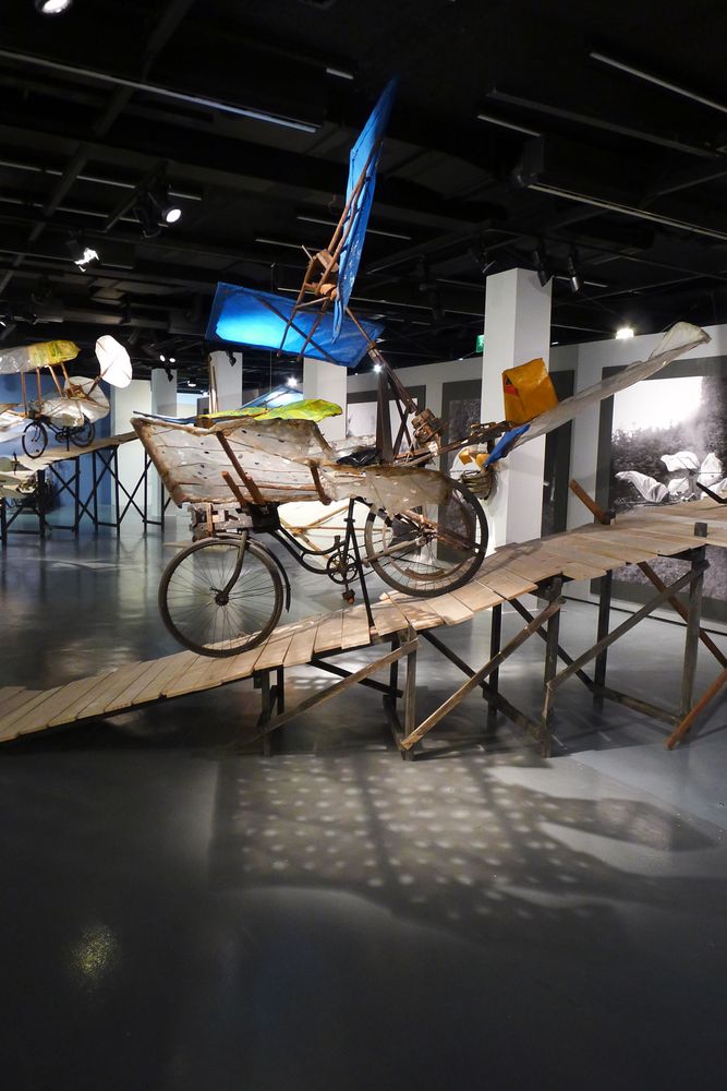 Die Ausstellungsansicht zeigt zwei Modelle von Flugrädern, die auf einer Holzrampe platziert sind.