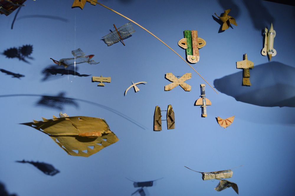 An einer blauen Wand hängen verschiedene kleine Flugmodelle aus Pappe.