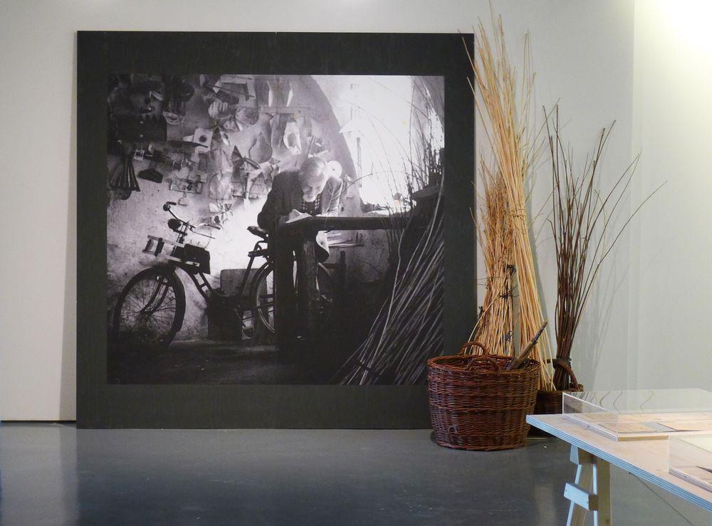 Die Ausstellungsansicht zeigt ein großes Porträt von Gustav Mesmer, welches an der Wand lehnt. Daneben stehen Körbe.