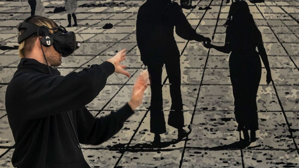 Ein schwarz gekleideter Mann kniet auf einem Bild, auf dem die schwarzen Silhouetten von mehreren Personen zu sehen sind. Er trägt eine VR-Brille und bewegt seine Arme.