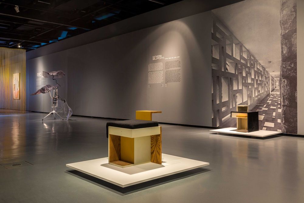 Die Ausstellungsansicht zeigt drei Installationen die im Raum aufgestellt sind. An der grauen Wand im Hintergrund befindet sich ein Ausstellungstext mit schwarz-weißer Schrift. 