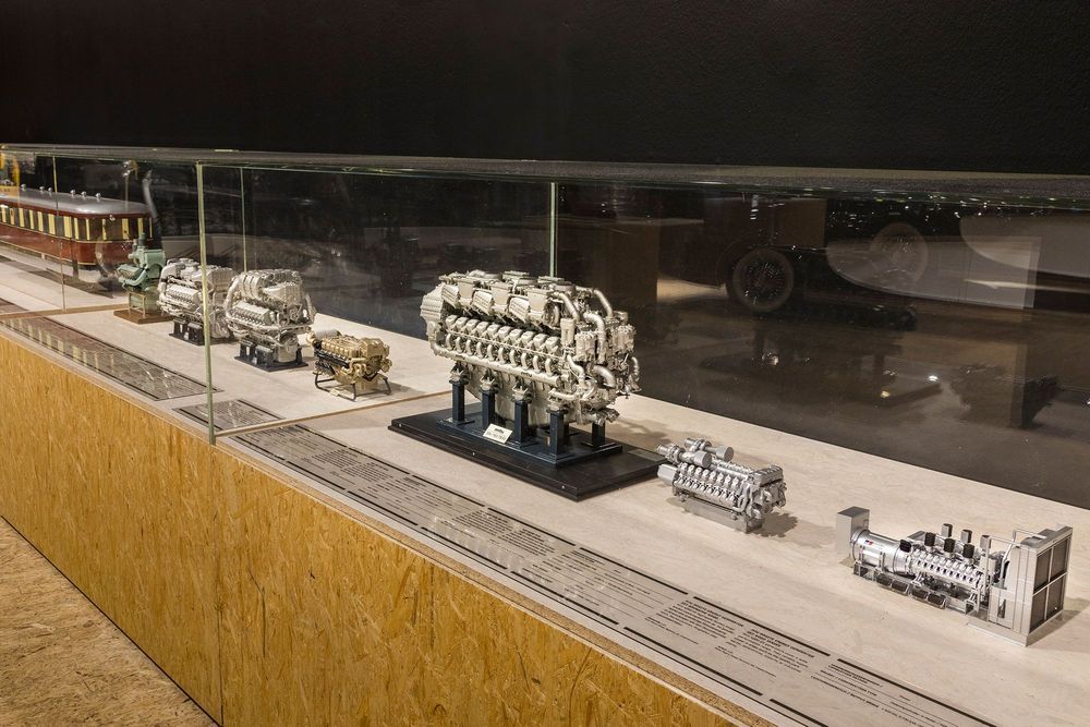 Die Ausstellungsansicht zeigt eine Reihe Vitrinen, in denen sich Antriebsmotoren in verschiedenen Größen befinden. Zusätzlich zu jedem Objekt ist ein kleiner Text vorhanden.