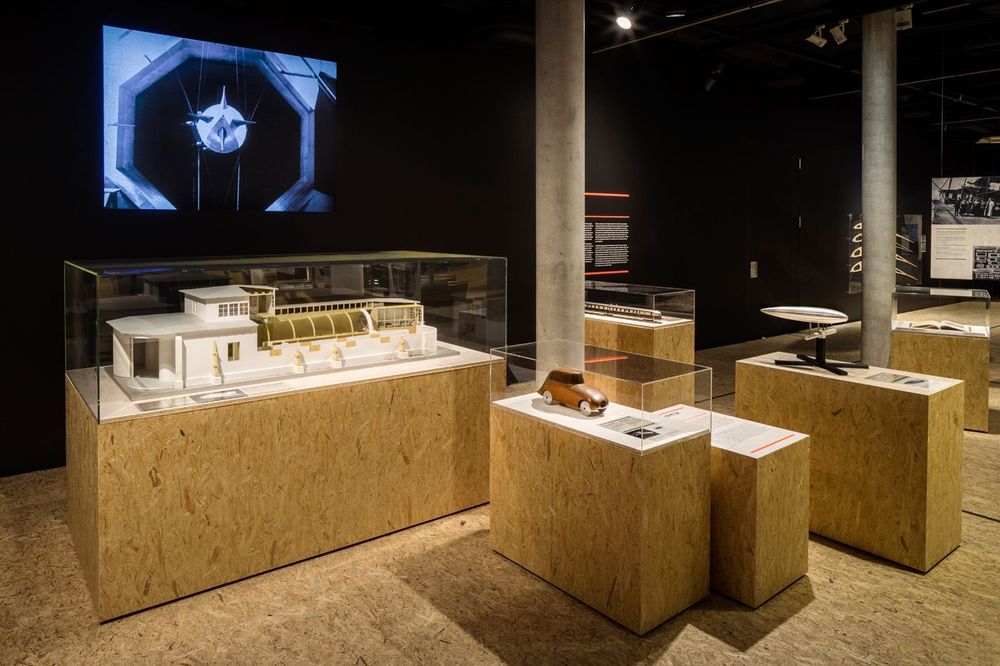 Die Ausstellungsansicht zeigt mehrere Holzpodeste und Kästen, auf denen sich Ausstellungsexponate unter einem Glaskasten befinden.