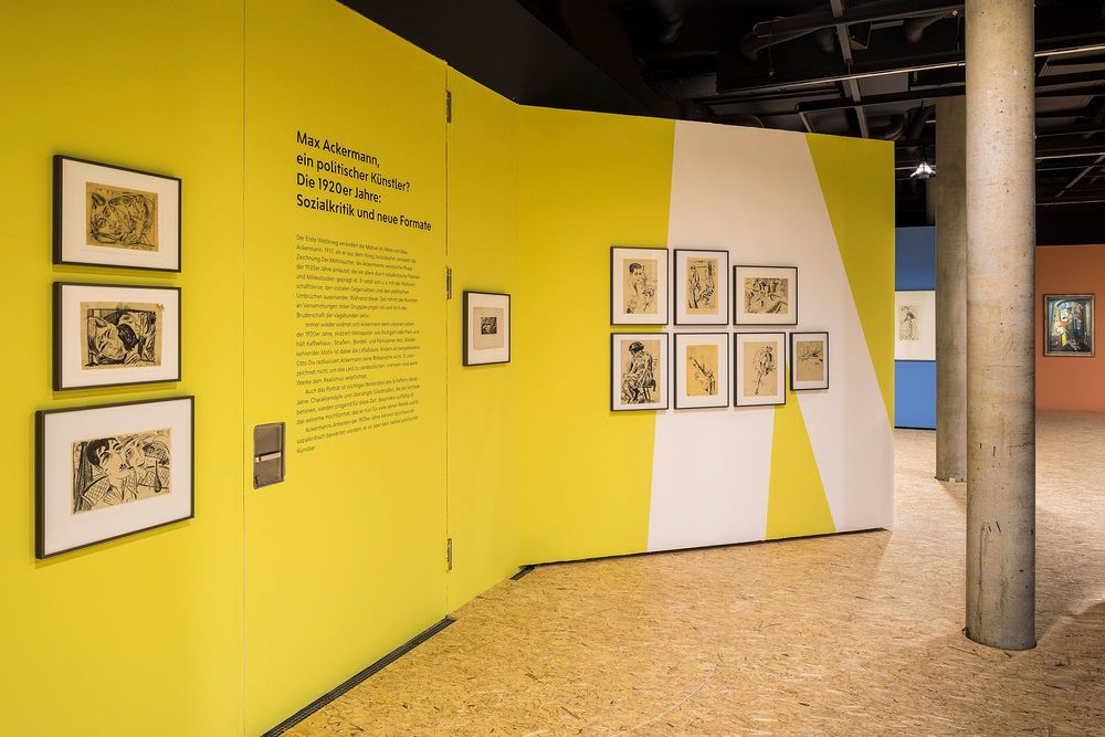 Die Ausstellungsansicht zeigt eine gelbe Wand, an der sich verschiedene Zeichnungen von Max Ackermann und ein Ausstellungstext befinden.
