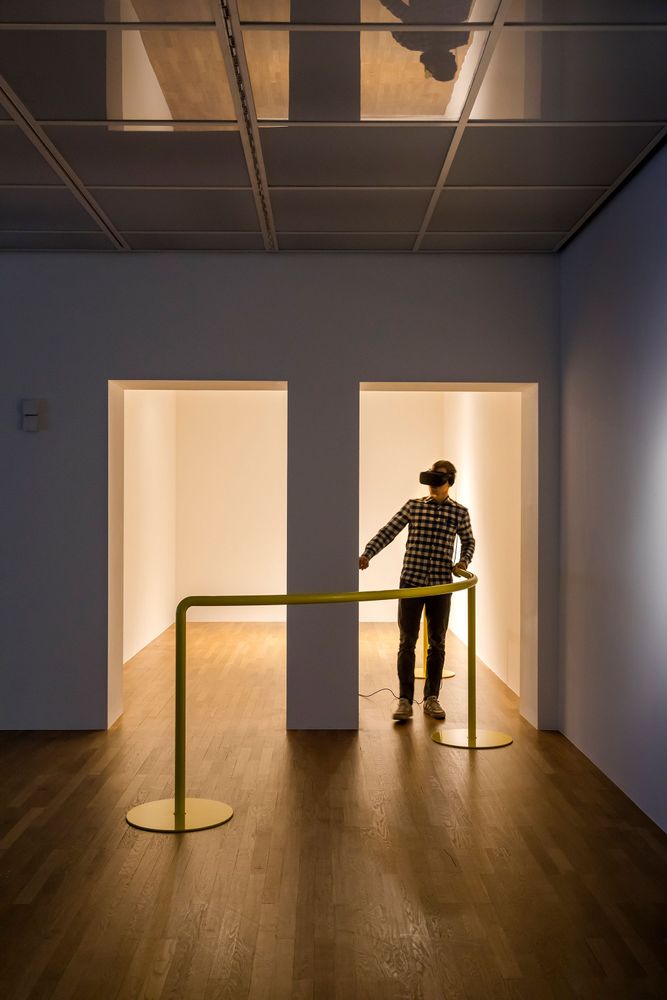 Ein Mann der eine VR-Brille trägt läuft, sich an einem gelben Geländer festhaltend, durch einen weißen Raum.