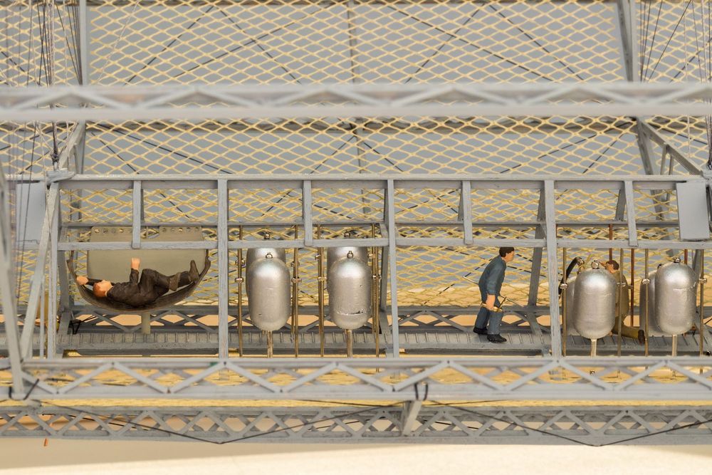 Die Aufnahme zeigt eine Detailansicht eines Luftschiffmodells. Drei kleine männliche Figuren arbeiten im Innenraum de Luftschiffs.