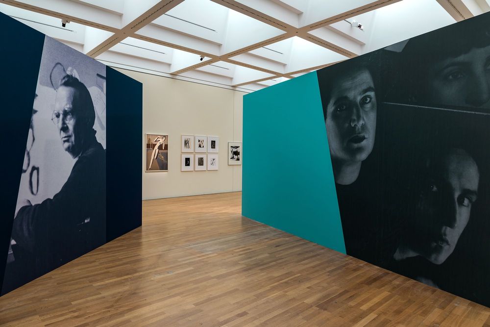 Die Ausstellungsansicht zeigt zwei breite Wände, die im Raum aufgestellt sind. An der vorderen Wand ist ein großes Porträt von Willi Baumeister abgedruckt. Auf der Wand daneben drei Porträtaufnahmen von Marta Hoepffner.