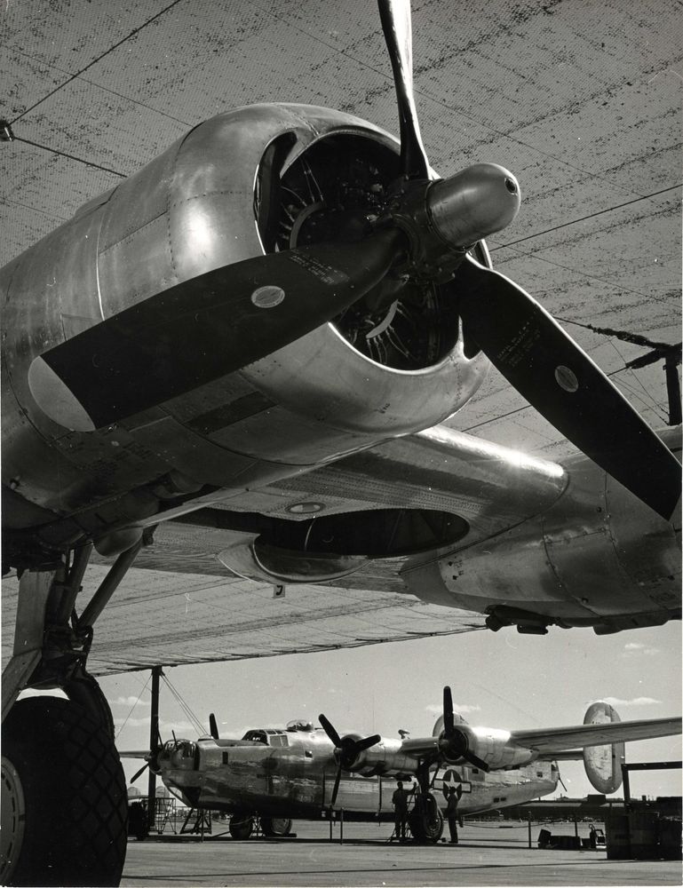 Die schwarz-weiß Fotografie zeigt die Nahaufnahme des Vorderseite eines Flugzeuges. Zu sehen sind die Propeller und ein Reifen. Im Hintergrund steht ein weiteres Flugzeug.