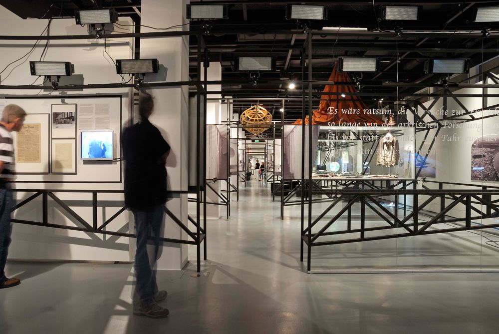 Die Ausstellungsansicht zu "66 Grad 30 Minuten Nord. Luftschiffe über der Arktis" zeigt zwei Personen, die Exponate in einer Vitrine betrachten.