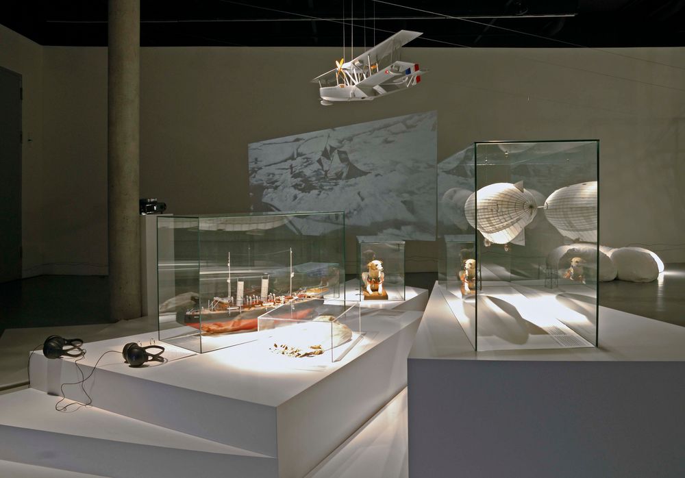 Die Ausstellungsansicht zu "66 Grad 30 Minuten Nord. Luftschiffe über der Arktis" zeigt zwei Vitrinen auf weißen Platten, die mit verschiedenen Exponaten und Modellen gefüllt sind.