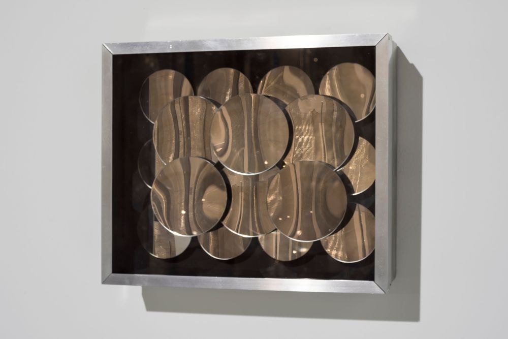 Eine Installation aus mehreren metallsichen Kreisen, die übereinander platziert sind, hängt in einem Rahmen. 