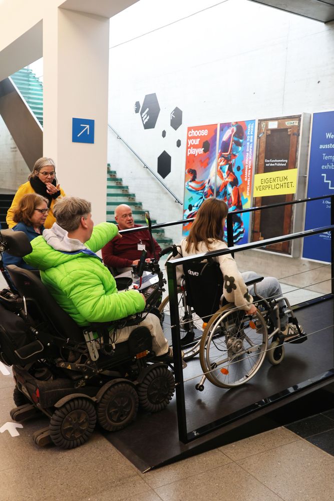 Jana Dix und Sabine Ochaba testen im Rollstuhl die Rampe zur Teilrekonstruktion der „Hindenburg“. Zwei Inkluencer und eine Mitarbeiterin von INIOS begleiten sie dabei. 
