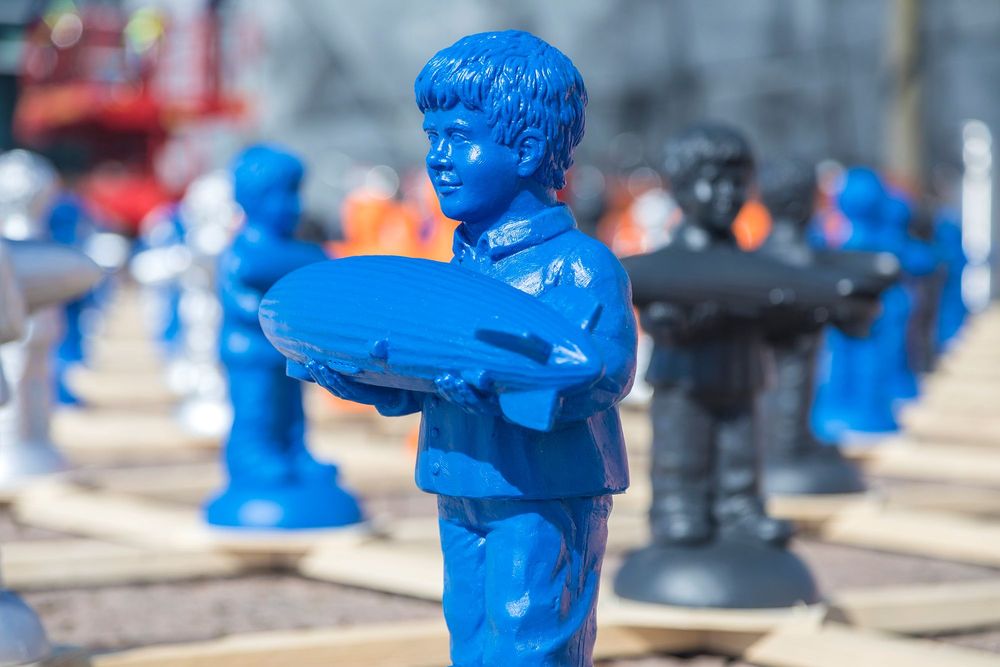 Auf einem Holzgitter sind an jedem Kreuzpunkt Figuren des Zeppelin Jungen befestigt. Die blaue Figur eines Jungen, der einen Zeppelin in beiden Händen hält.