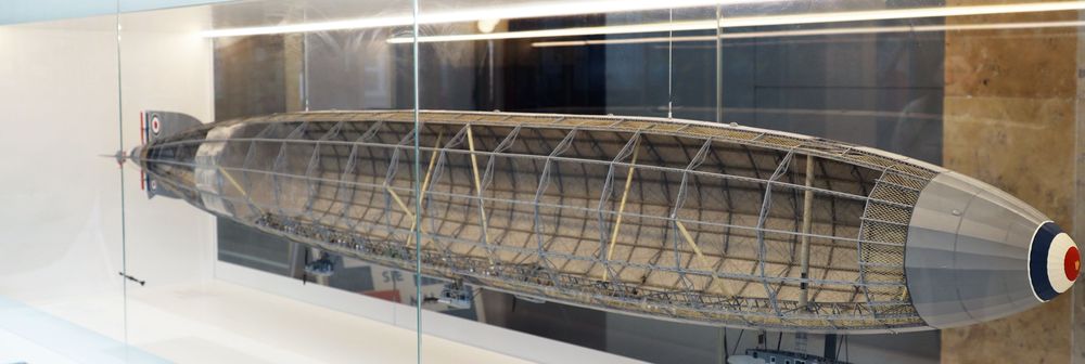 Modell eines Zeppelins in einer Glasvitrine, mit sichtbarem Gerüst und detaillierter Innenstruktur. Die Spitze des Luftschiffs zeigt eine runde Markierung in Blau, Weiß und Rot.