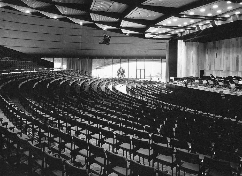 Die schwarz-weiß Fotografie zeigt einen großen Saal in dem Unmengen an Stühlen aneinandergereiht stehen.