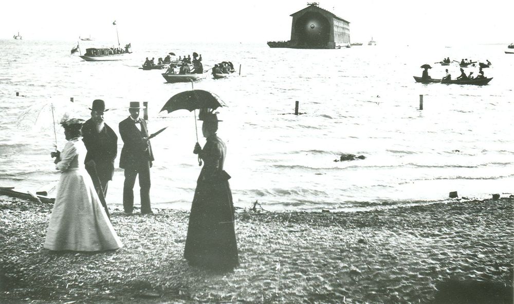 Königin Charlotte und König Wilhelm II. von Württemberg stehen mit zwei Begleitpersonen am Ufer des Bodensees und beobachten den Erstaufstieg des LZ 1.