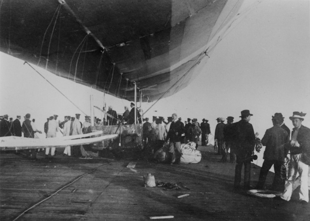 Das Foto wurde auf den Pontons aufgenommen. Man sieht den Bauch des Zeppelins und eine große Anzahl von Gästen. In einer Gondel stehen einige Menschen.