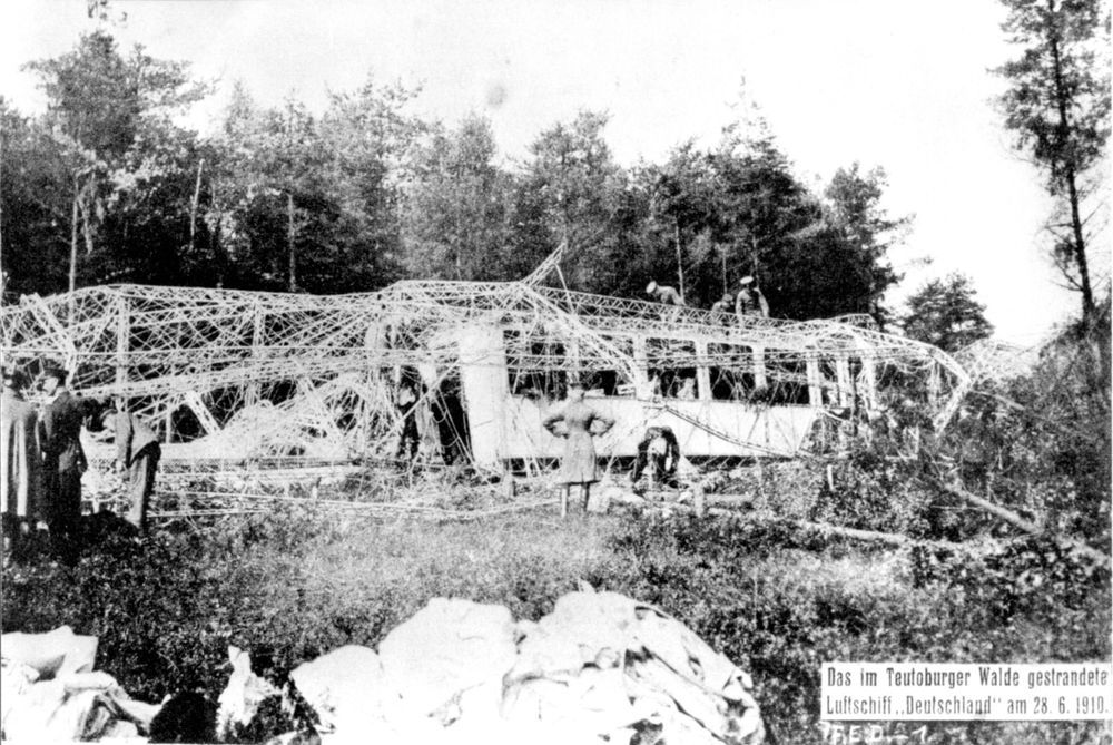 LZ 7 „Deutschland“ steckt im Wald fest. In der Mitte sieht man die Gondel, darüber das Aluminiumgerippe, das gerade von einigen Männern abgebaut wird.