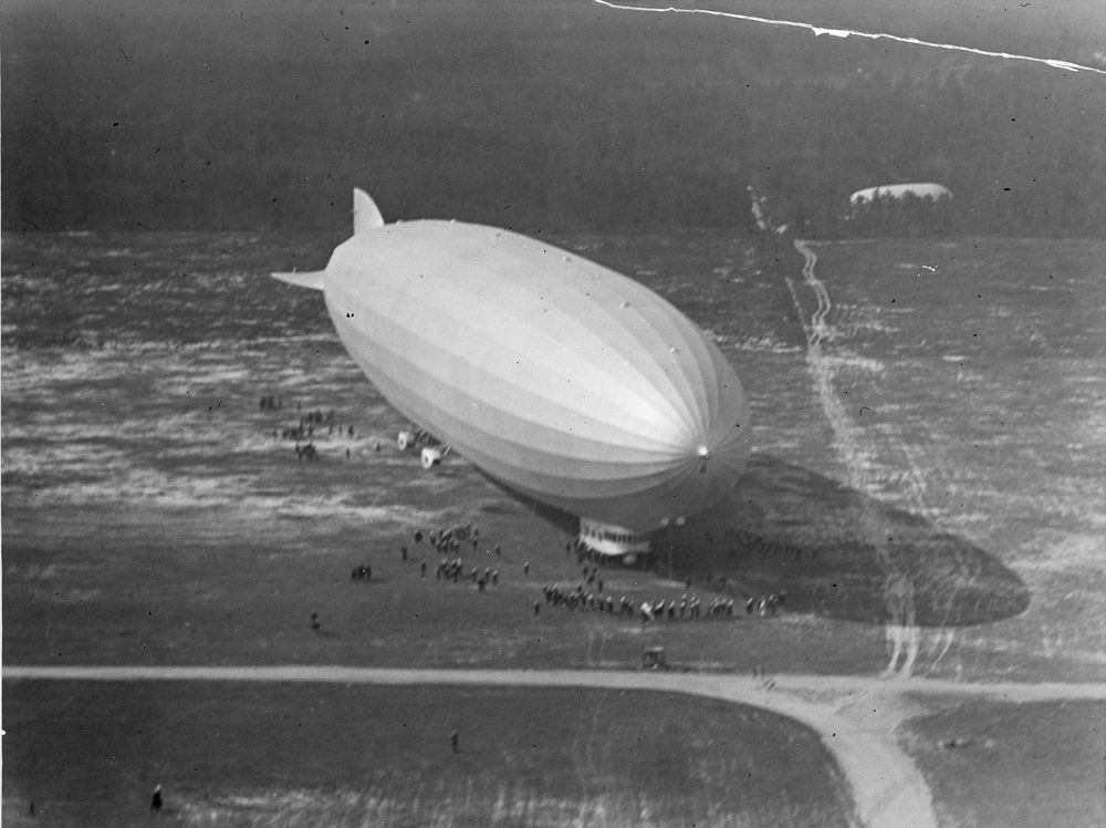 LZ 126 kurz nach der Landung auf dem Flugfeld in Lakehurst. Der Blick fällt aus der Vogelperspektive direkt auf das Flugfeld, auf dem viele Menschen stehen. 