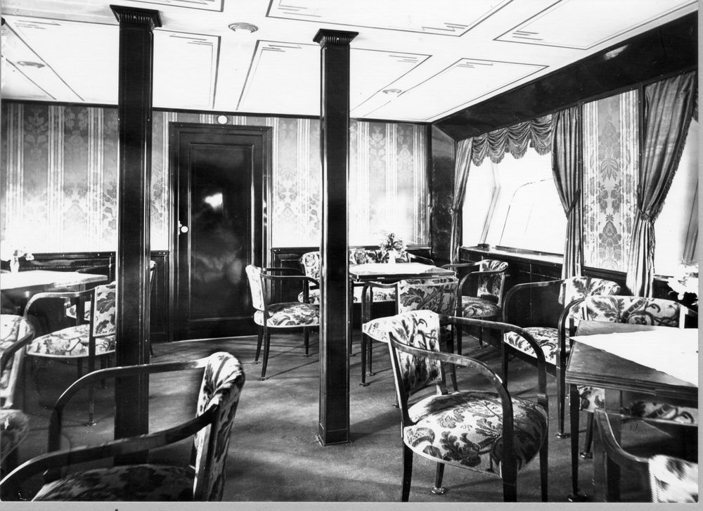 Die historische Aufnahme zeigt die Inneneinrichtung eines Aufenthaltsraum im Zeppelin. Im Raum sind mehrere Tische und Stühle verteilt.