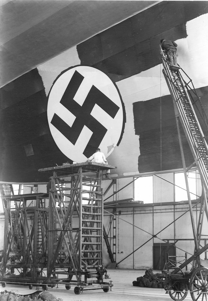 Ein historisches schwarz-weiß Foto vom unteren Seitenleitwerk des Zeppelins. Auf das Leitwerk wird gerade mit Hilfe großer Leitern das Hakenkreuzsymbol des NS-Staats aufgemalt.