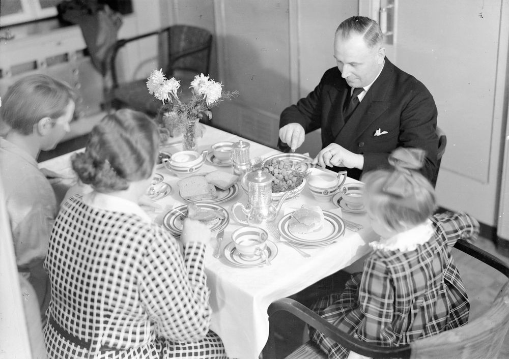 Die historische Aufnahme zeigt eine vierköpfige Familie die an einem Esstisch sitzt. 