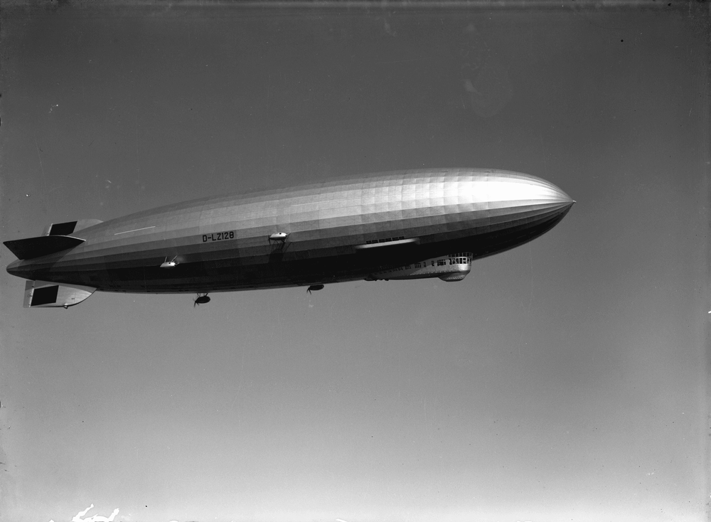 Ein großer Zeppelin in der Luft vor einem klaren Himmel. Unter dem Zeppelin befindet sich eine Gondel mit Fenstern.