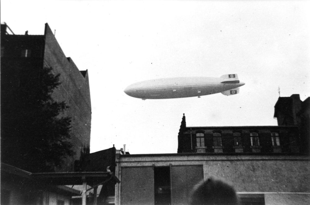 Schwarz-weiß Foto: LZ 129 „Hindenburg“ fährt in Berlin über das Gebäude des Deutschen Kurzwellensenders. Unterschiedliche Häuser stehen im Vordergrund.