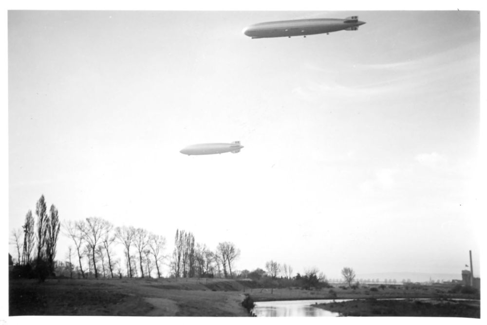 Schwarz-Weiß-Foto der beiden Luftschiffe in der Nähe von Düren. Unterhalb der Zeppelin, die parallel zu einander fahren, liegt eine Flusslandschaft.