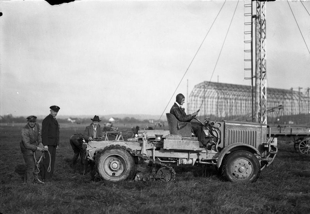 Die historische Aufnahme zeigt einen Raupenschlepper, ein Fahrzeug das damals den hohen personellen Aufwand bei Zeppelinlandungen verringern sollte. Das Fahrzeug wird von einem Mann gesteuert.