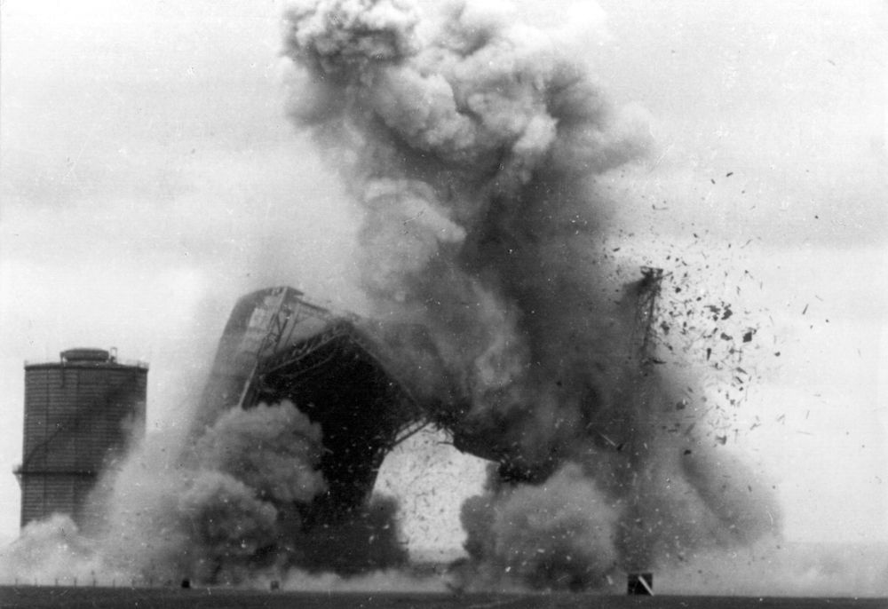 Eine große Explosion zeigt die Sprengung der Halle. Schutt und Staub werden weit in den Himmel geschleudert, die Halle komplett zerstört. 