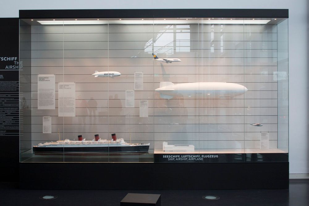 Blick auf die Vitrine mit LZ 129 Modell. Darum herum verschiedene Modelle, unter anderem des Schiffs Queen Mary und des Hafenbahnhofs. Um das Modell herum sind das Flugzeug Airbus A380, ein Zeppelin NT und eine Boeing Dixi Clipper.