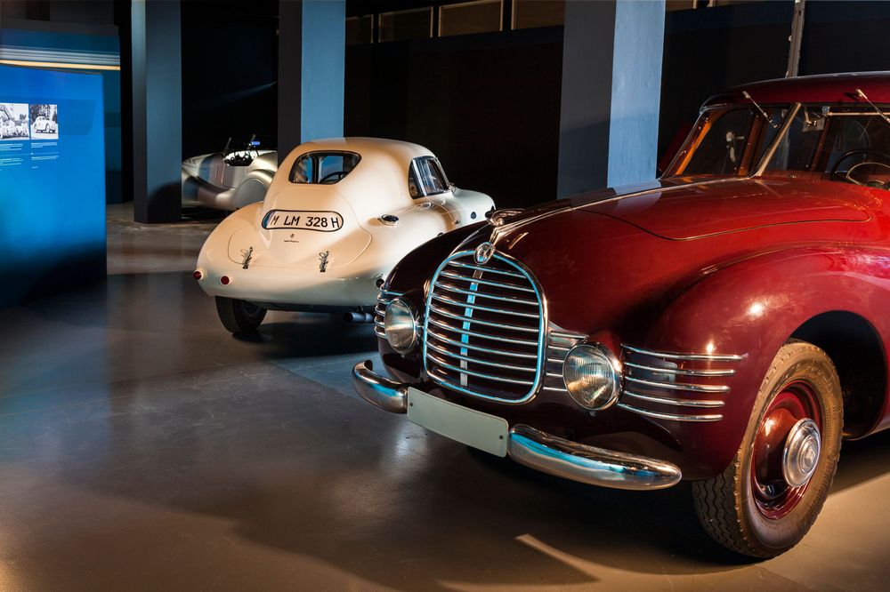 Die Ansicht zeigt einen roten Oldtimer der Marke Horch, dahinter steht ein weiteres altes Auto in weiß.
