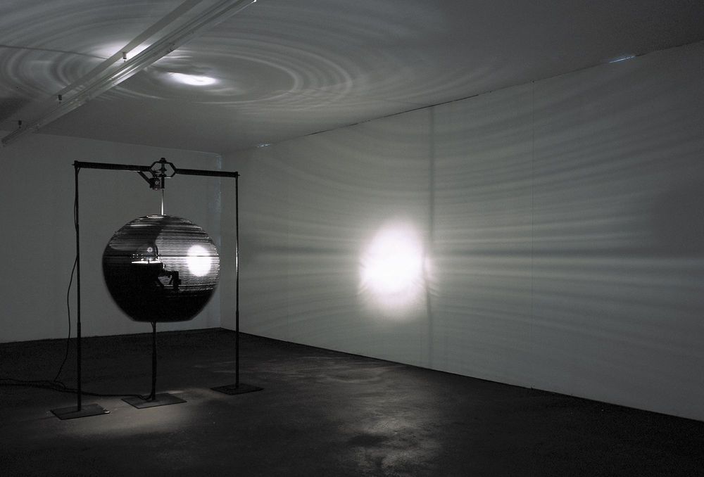 Schwarz-weiß Aufnahme einer kugelförmigen Installation, die sich in einem leeren Raum befindet.