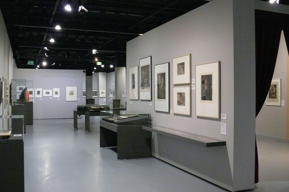 Die Ausstellungsansicht zu "Gestochen scharf" zeigt einen Bereich mit vielen Vitrinen und Bilderrahmen an den Wänden. 