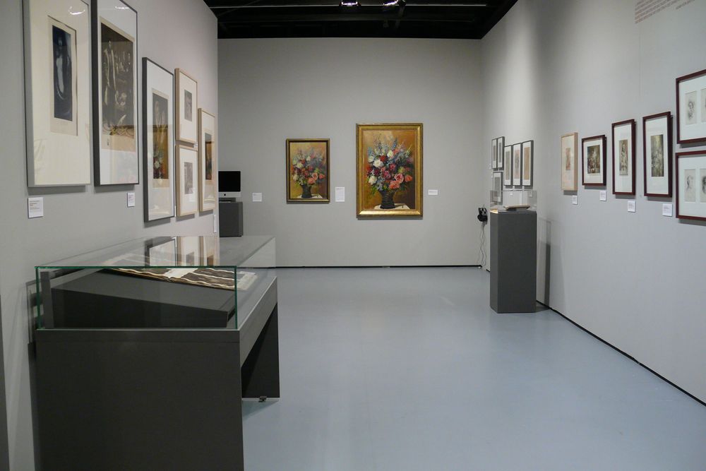 Die Ausstellungsansicht zu "Gestochen scharf" zeigt einen Gang mit einer großen Vitrine links im Vordergrund. Im Hintergrund befindet sich eine weitere Vitrine und an allen Wänden hängen sehr viele Bilderrahmen.