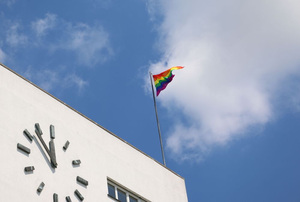 Eine Regenbogenfahne weht am Mast auf dem Zeppelin Museum. Im Hintergrund sieht man den blauen Himmel mit Wolken.